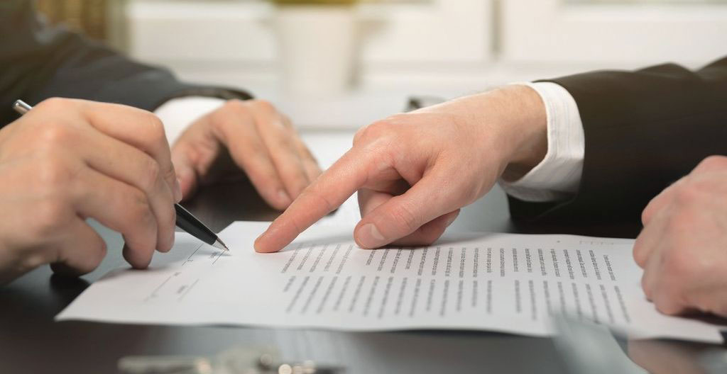 Gros plan d'une main masculine tenant un stylo-plume bleu marine, apposant une mention manuscrite sur un contrat de mandat exclusif immobilier imprimé en français